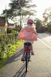 Girl wearing pink helmet riding bicycle along street - FOLF07684