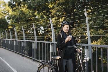 Young woman standing by bicycle using phone - FOLF07699