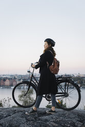 Young woman standing by bicycle on rock - FOLF07701