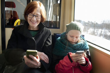 Mädchen mit Großmutter sitzt in der Straßenbahn und benutzt Smartphones - FOLF07750