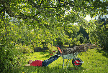 Man lying on grass with legs on wheelbarrow - FOLF07811
