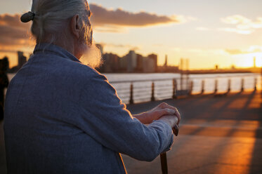Älterer Mann sitzt bei Sonnenuntergang auf der Promenade - CAVF33490
