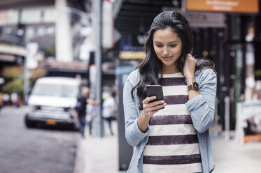 Junge Frau, die auf dem Gehweg eine SMS schreibt - CAVF33495