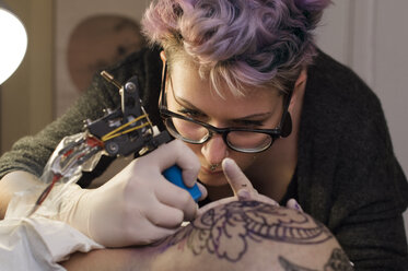 Female tattoo artist tattooing head of client in studio - CAVF33539