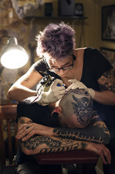 Female tattoo artist tattooing male client in studio - CAVF33540