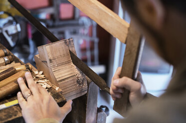 Cropped image of man cutting wood with hand saw in workshop - CAVF33544