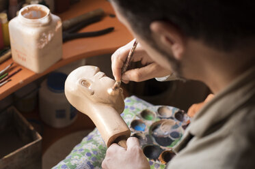 High angle view of man painting figurine in workshop - CAVF33547