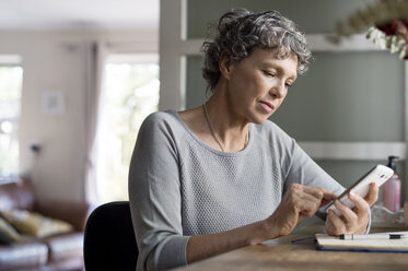 Reife Frau benutzt Smartphone bei der Arbeit zu Hause - CAVF33561