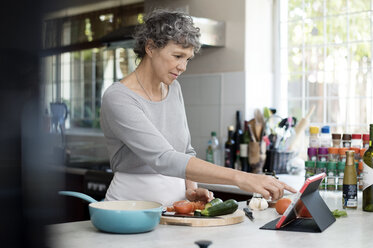 Reife Frau benutzt digitales Tablet beim Kochen in der Küche - CAVF33565
