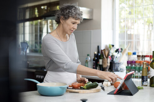 Mature woman using digital tablet while cooking in kitchen - CAVF33565