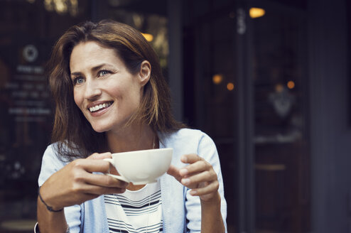 Glückliche Frau, die mit einer Kaffeetasse in der Hand in einem Straßencafé wegschaut - CAVF33580