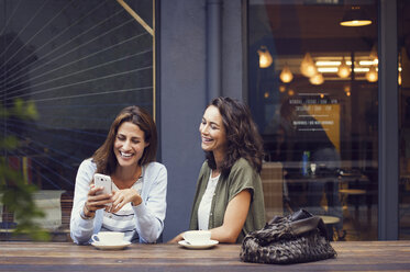 Glückliche Freundinnen benutzen ihr Smartphone in einem Straßencafé - CAVF33583