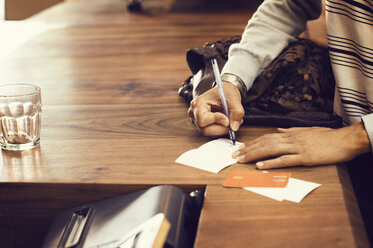 Midsection of female customer signing bill at checkout counter in cafe - CAVF33590