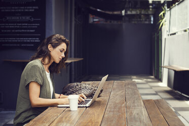 Side view of woman using laptop at sidewalk cafe - CAVF33592