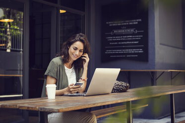 Happy woman using smart phone while sitting at sidewalk cafe table - CAVF33593