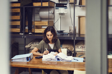 Mature female owner analyzing documents at table in coffee shop - CAVF33598