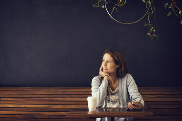 Nachdenkliche Frau, die am Tisch eines Cafés sitzt und wegschaut - CAVF33604