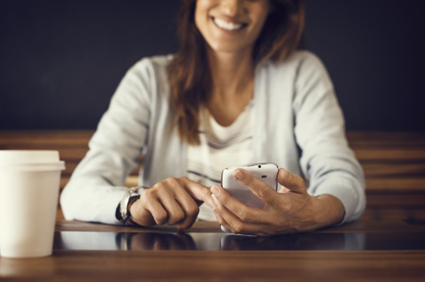 Mittelteil einer lächelnden Frau, die in einem Café ein Mobiltelefon benutzt, lizenzfreies Stockfoto