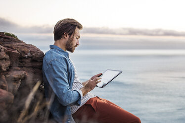 Seitenansicht eines Mannes, der einen Tablet-Computer am Meer benutzt - CAVF33639