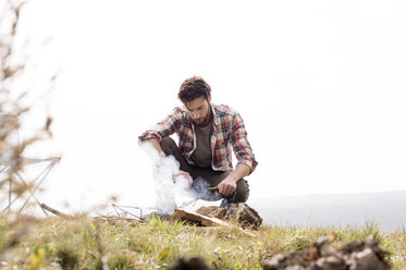 Man preparing tea on bonfire at campsite against clear sky - CAVF33662