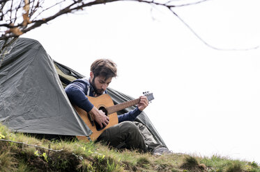 Mann spielt Gitarre vor einem Zelt auf einem Hügel gegen den klaren Himmel - CAVF33669