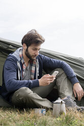 Mann benutzt Smartphone außerhalb des Zeltes auf einem Hügel gegen den klaren Himmel - CAVF33671