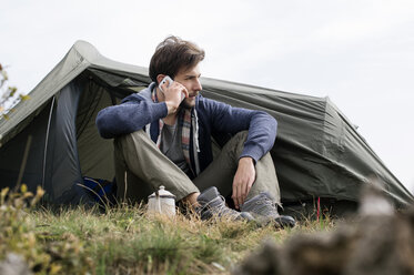 Mann, der vor einem Zelt auf einem Hügel bei klarem Himmel an sein Smartphone geht - CAVF33672