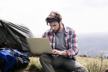 Mann mit Laptop auf einem Campingplatz auf einem Hügel gegen den klaren Himmel - CAVF33676