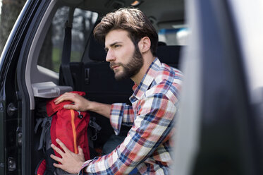 Side view of thoughtful man sitting in car trunk - CAVF33677