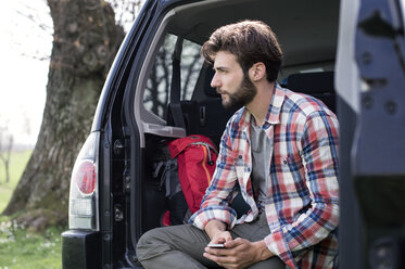 Nachdenklicher Mann sitzt im Kofferraum eines Autos auf dem Campingplatz - CAVF33678