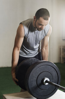 Männlicher Sportler, der eine Langhantel im Fitnessstudio befestigt - CAVF33696