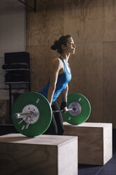 Seitenansicht eines entschlossenen weiblichen Athleten, der eine Langhantel im Fitnessstudio hebt - CAVF33698