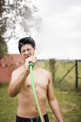 Shirtless man spraying water on face at yard - CAVF33713