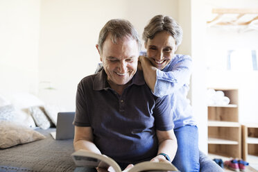 Fröhliches älteres Paar, das im Schlafzimmer ein Buch liest - CAVF33727