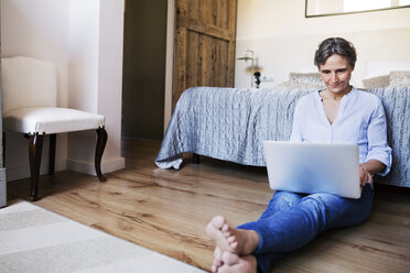 Reife Frau benutzt Laptop, während sie im Schlafzimmer auf dem Boden sitzt - CAVF33732