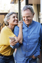 Cheerful woman looking at senior man using smart phone on porch - CAVF33760
