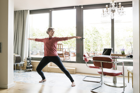 Mature woman practicing yoga in Warrior 2 pose at home stock photo