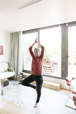 Ältere Frau übt Yoga in Baumhaltung zu Hause, lizenzfreies Stockfoto