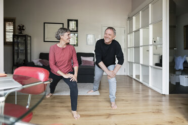 Happy senior couple doing stretching exercise at home - CAVF33782