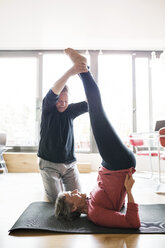 Senior man assisting woman in exercising at home - CAVF33788