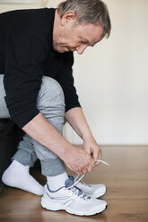 Senior man wearing sports shoes at home - CAVF33792