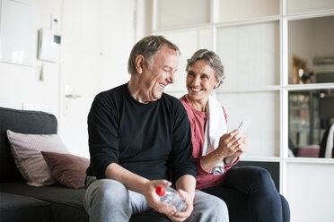 Glückliches älteres Paar, das ein Smartphone im Wohnzimmer benutzt - CAVF33801