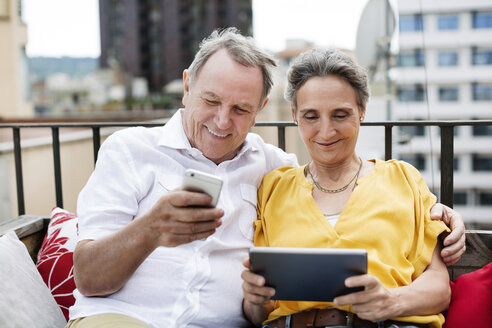 Glückliches älteres Ehepaar benutzt Smartphone und Tablet-Computer auf der Terrasse - CAVF33806