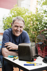 Porträt eines glücklichen älteren Mannes, der ein altes Radio auf dem Hof repariert - CAVF33826