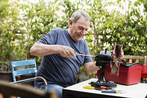Glücklicher älterer Mann, der einen elektrischen Ventilator auf dem Hof repariert - CAVF33828