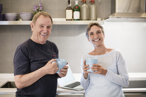 Porträt eines glücklichen älteren Paares mit Kaffeetassen in der Küche, lizenzfreies Stockfoto