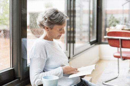 Seitenansicht einer reifen Frau, die zu Hause ein Buch liest - CAVF33838