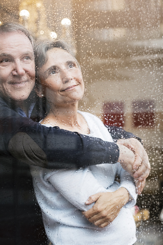 Verliebtes älteres Paar schaut durch ein nasses Fenster, lizenzfreies Stockfoto