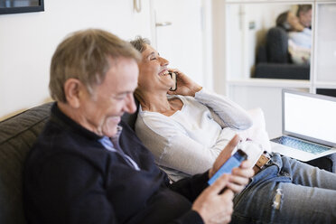 Glückliches älteres Paar benutzt Smartphones im Wohnzimmer - CAVF33852