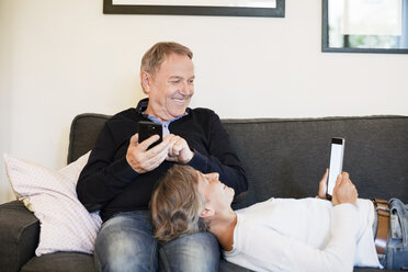 Happy senior couple using tablet computer on sofa - CAVF33855